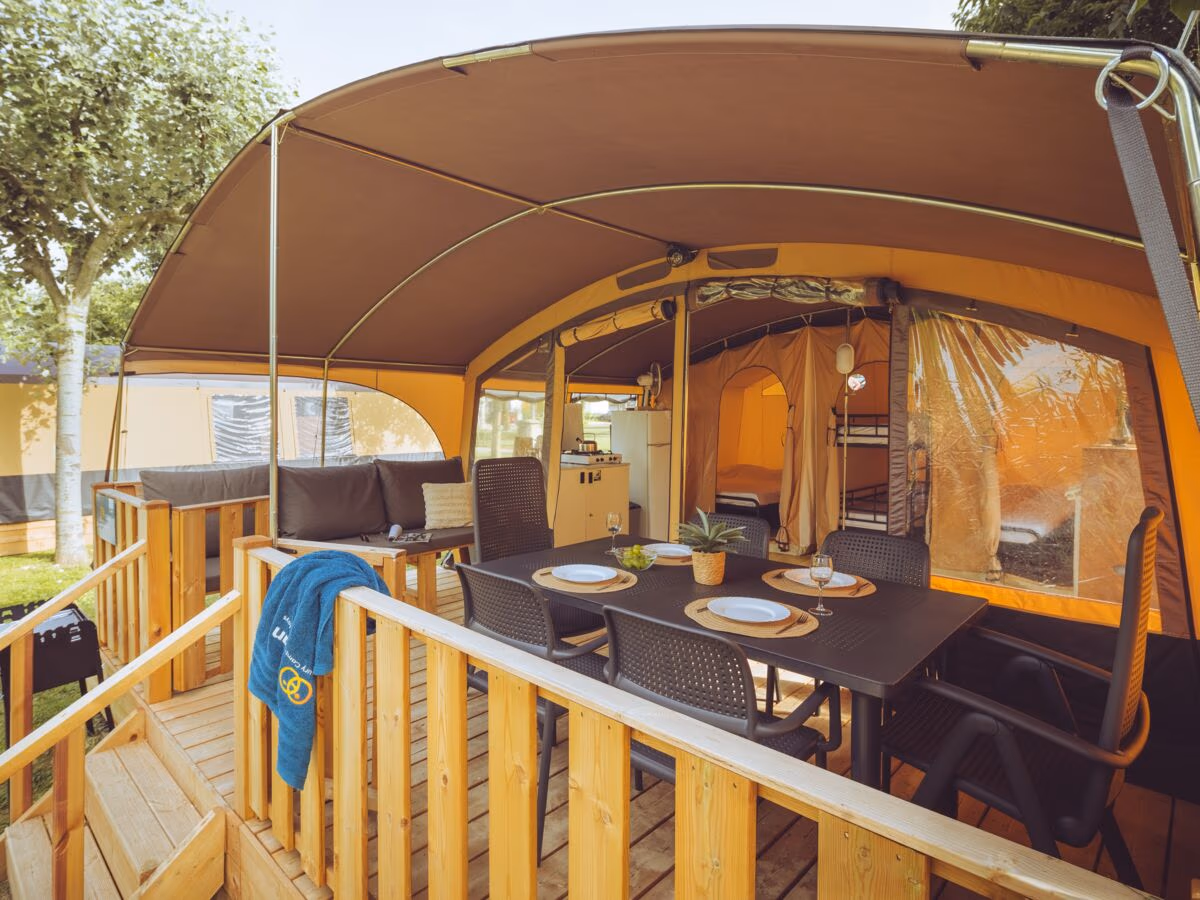 Lodgetent Holiday met een gebogen dak en een overdekt terras met eettafel voor zes, met de keuken en een stapelbed erachter