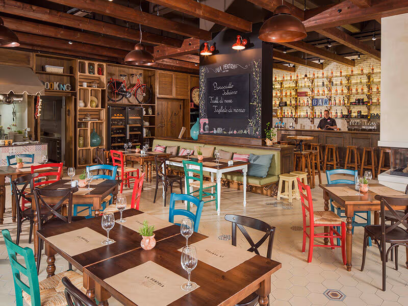 Het kleurrijke interieur van trattoria La Pentola op Camping Lanterna, met bar en gedekte tafels
