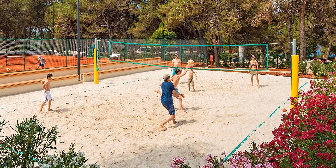 Vakantiegangers spelen beachvolleybal op het zandveld van het sportpark, Camping Lanterna