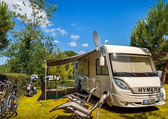 Ruime Comfort-kampeerplaats met camper onder groene bomen op Camping Lanterna