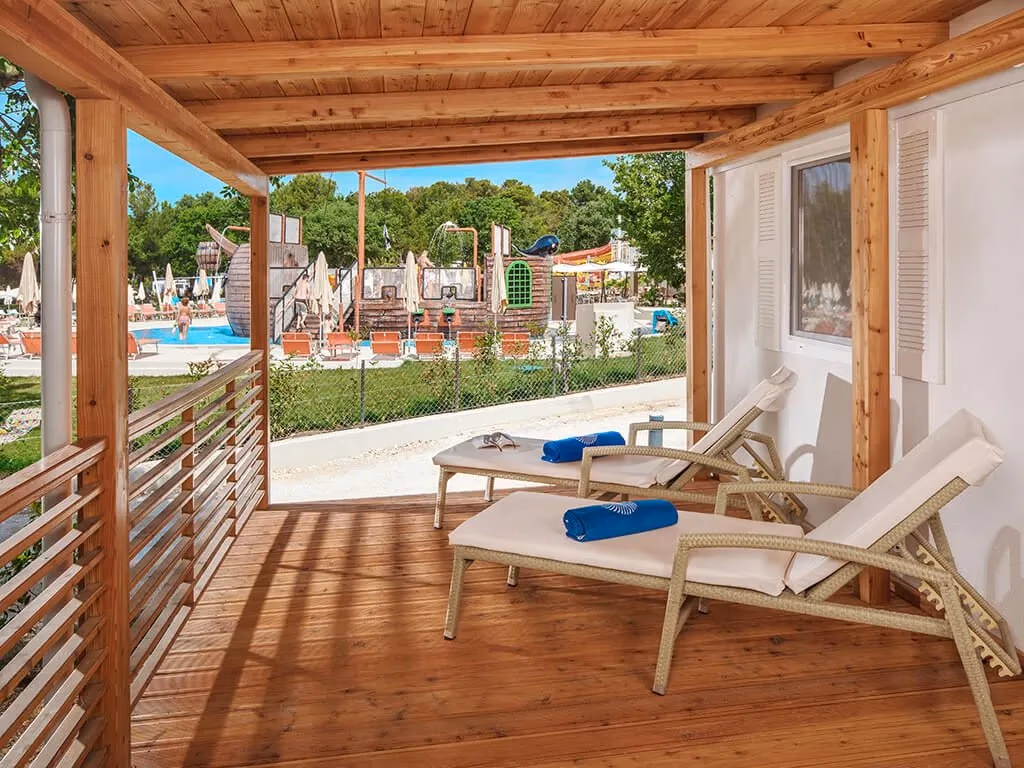 Overdekt terras van een Istrian Home op Camping Lanterna met twee ligbedden en uitzicht op het piratenzwembad