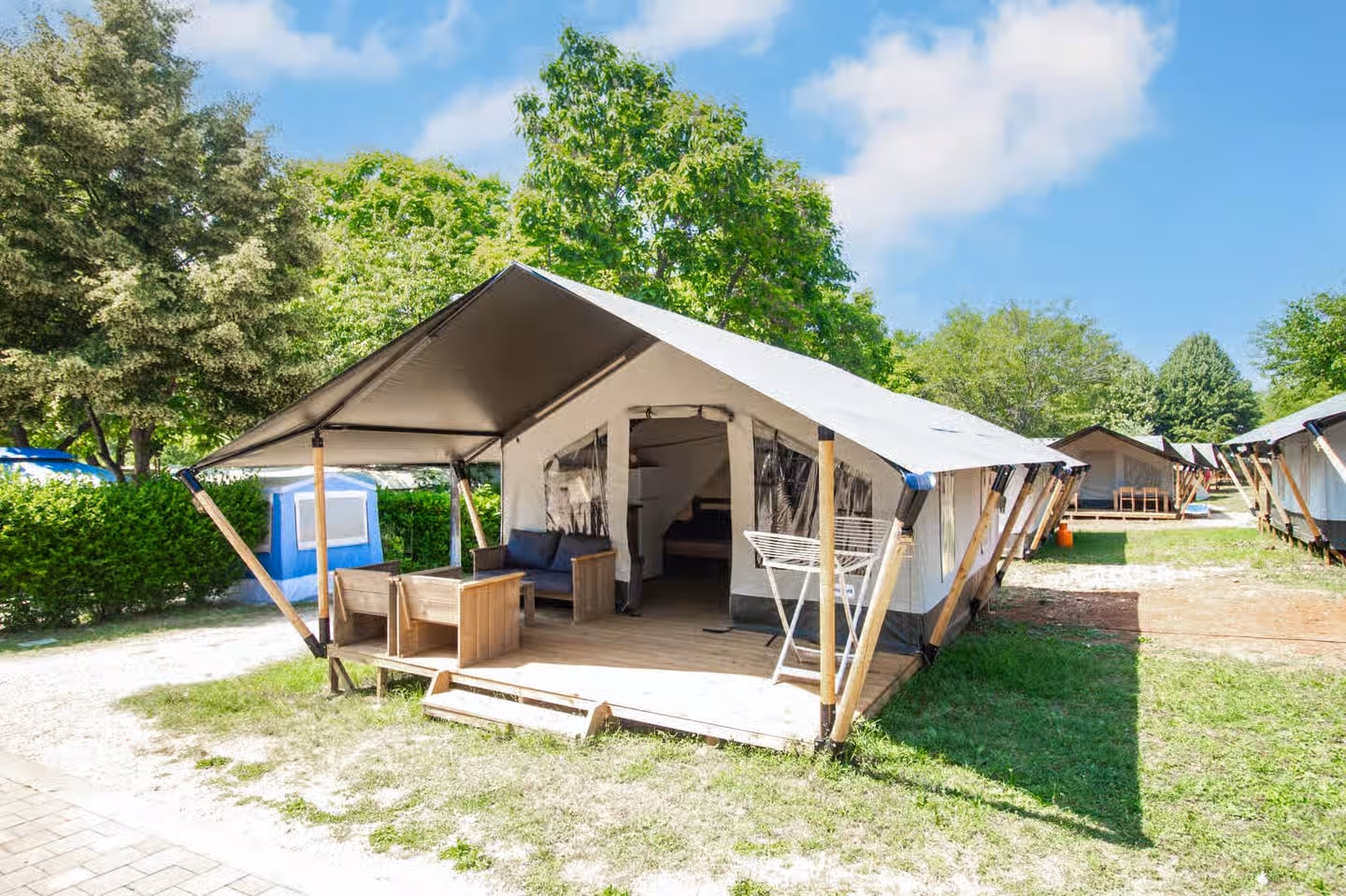 Safaritent met een luifel op houten palen, loungestoelen op het terras en een droogrek, op een grasveldje