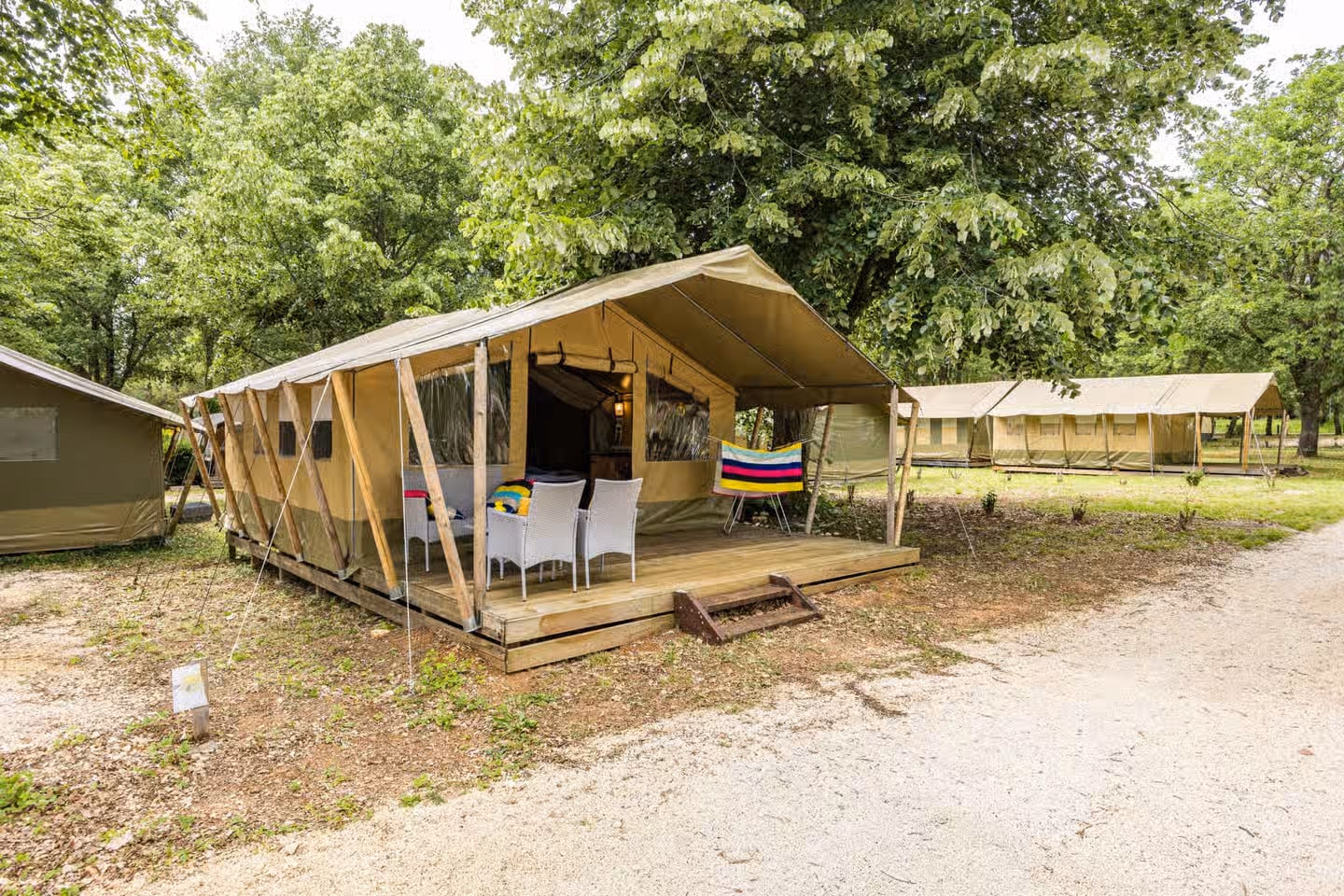 Safaritent Harmony op Camping Lanterna met witte stoelen aan een tafel op het terras en een gekleurde handdoek over de reling