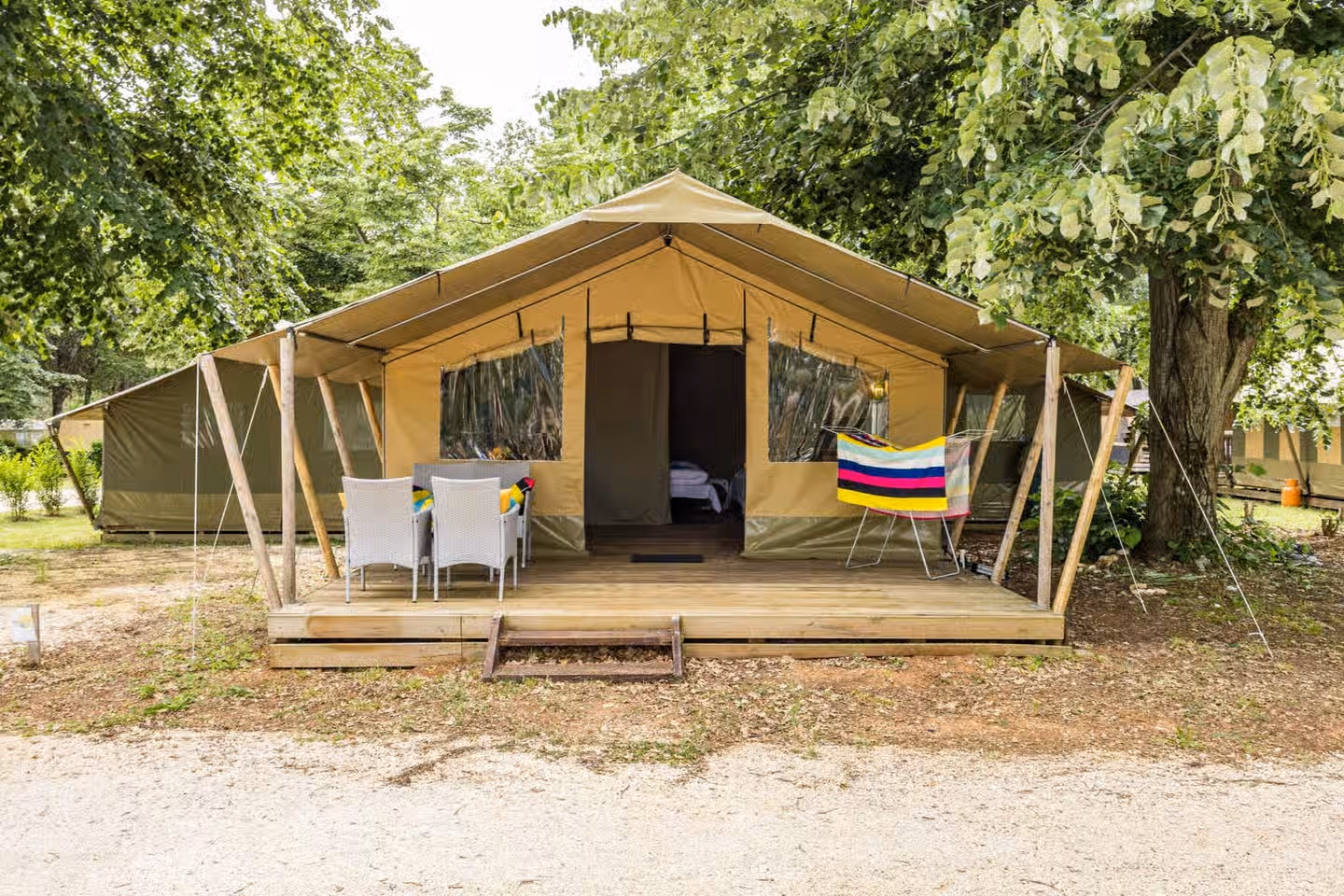 Safaritent Harmony op Camping Lanterna met witte stoelen aan een tafel op het terras en een gekleurde handdoek over de reling