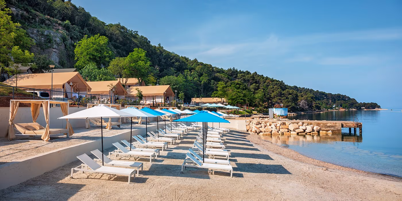 Kiezelstrand met ligbedden, parasols en glampingtenten aan de baai van Camping Lanterna