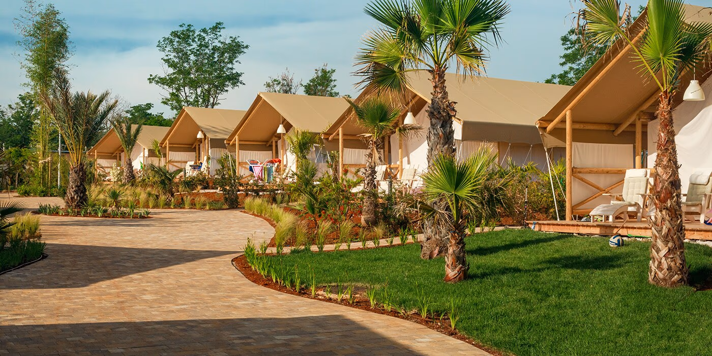 Glampingtenten langs een groen pad met palmbomen in Maro Village, Camping Lanterna