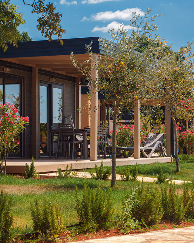 Mobile home met houten terras tussen olijfbomen en bloeiende oleanders op Camping Lanterna in Istrie