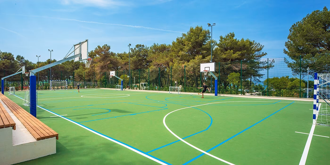 Groen multifunctioneel sportveld tussen de bomen van Camping Lanterna