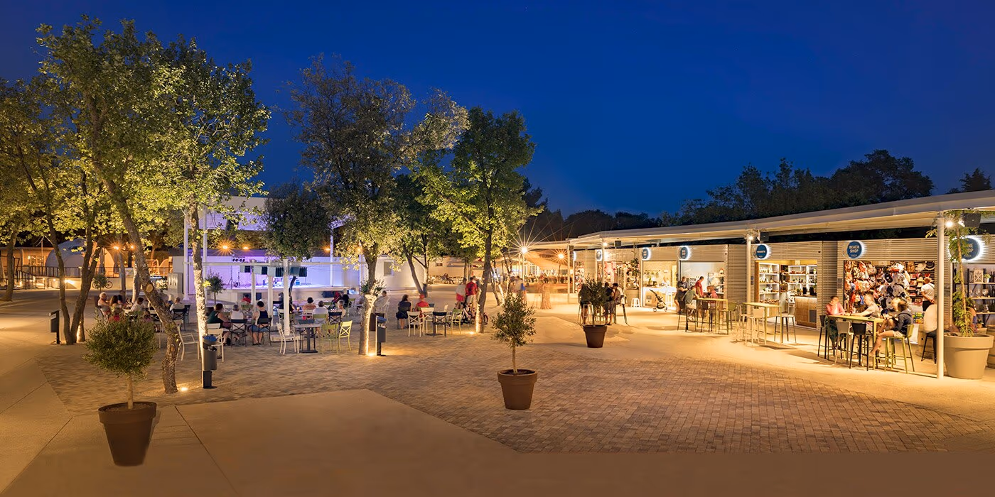 Levendig centraal plein met winkels en terrasverlichting in de avond op Camping Lanterna