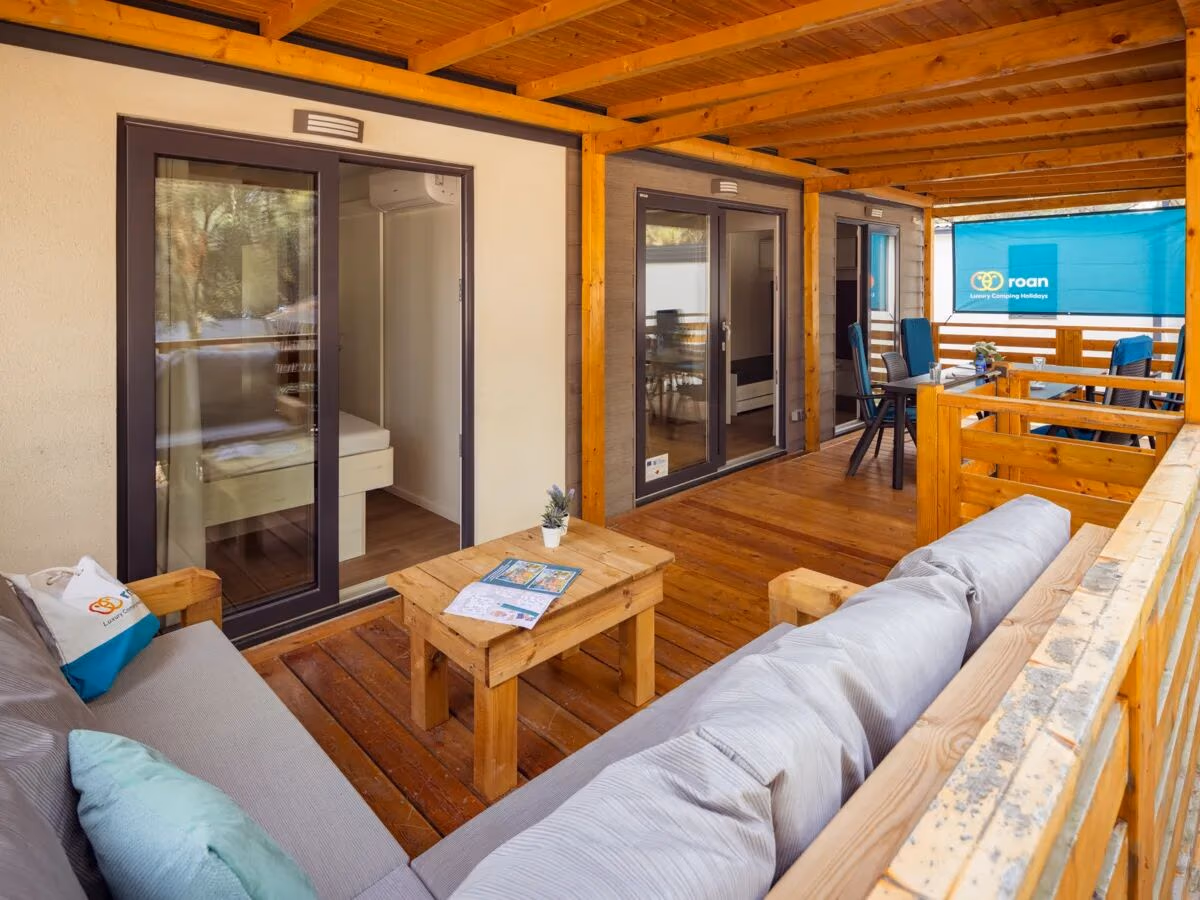 Veranda van een Comfort Plus Lounge op Camping Lanterna, met loungebank, houten salontafel en schuifdeuren naar de woonruimte