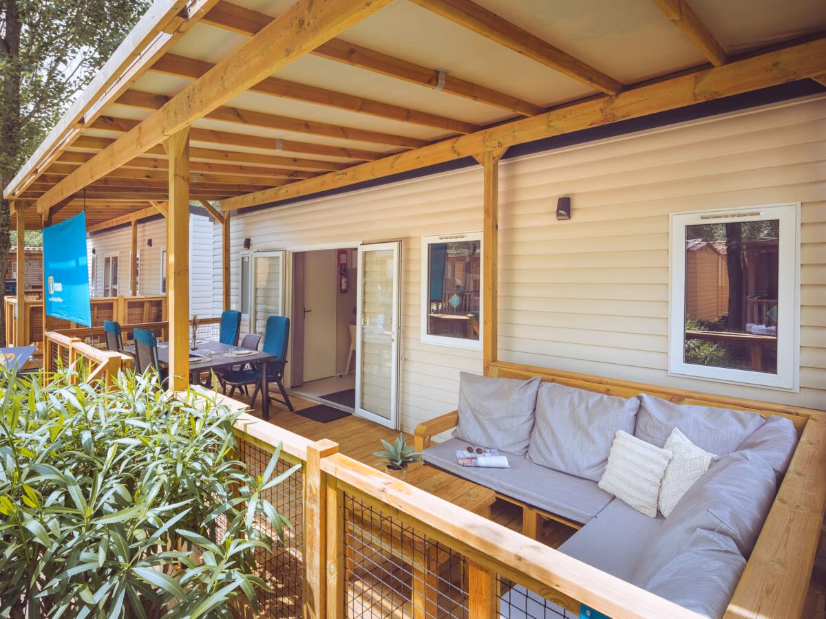 Overdekte veranda van een Premium Lounge-stacaravan, met een grijze loungebank en een eettafel met blauwe stoelen