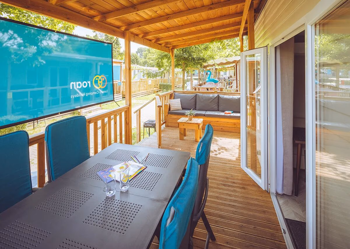 Houten veranda van een Premium Relax-stacaravan op Camping Lanterna, met eettafel, blauwe stoelen en een loungebank verderop