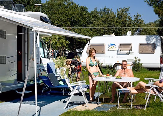 Gezin bij een caravan op een groene standaardkampeerplaats van Camping Lanterna