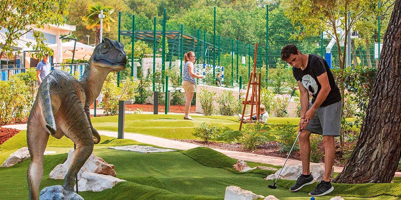 Spelers bij een dinosaurusdecor op de Terra Magica-minigolfbaan van Camping Lanterna