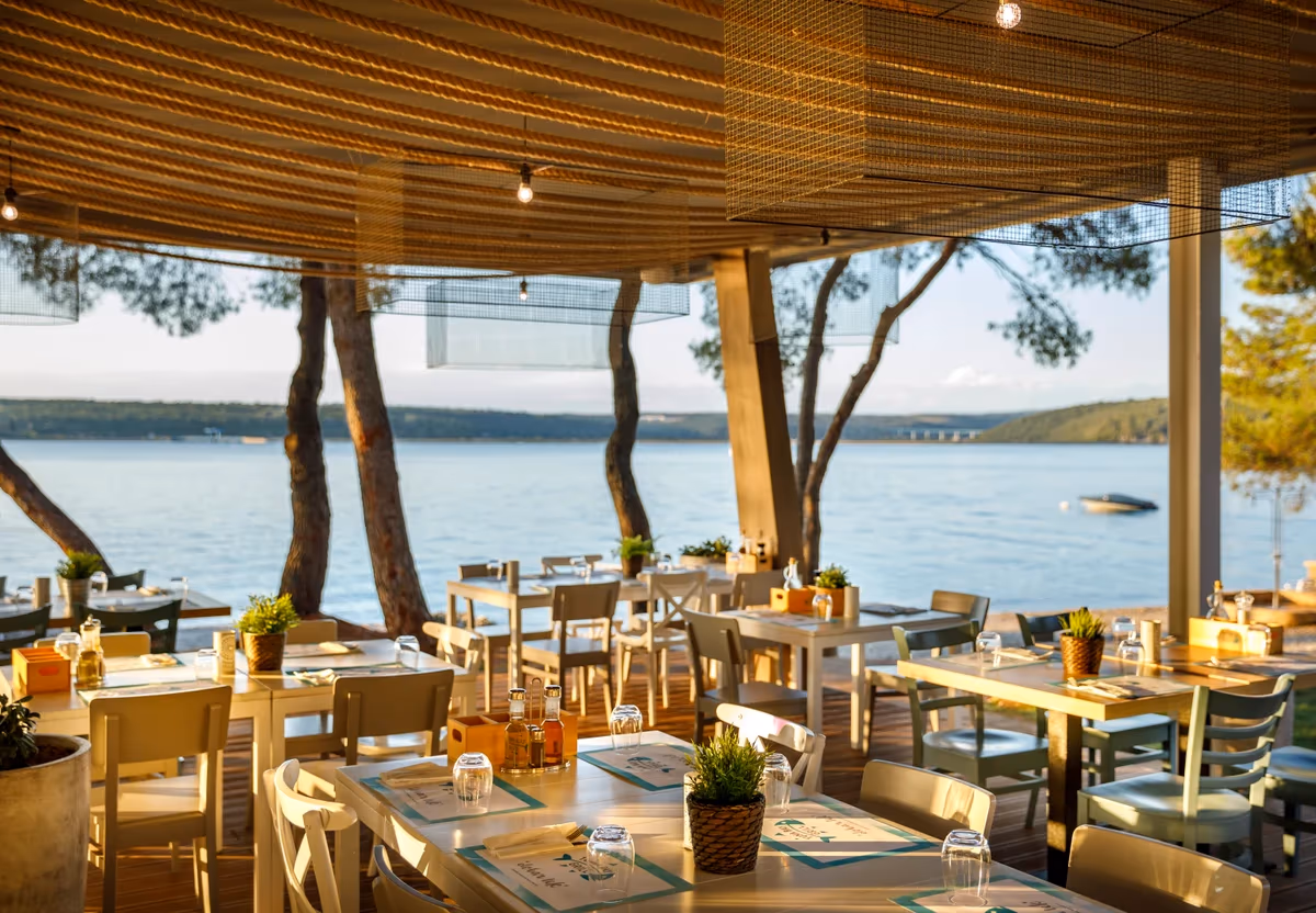 Restaurantterras onder een houten pergola aan het water bij zonsondergang op Camping Lanterna