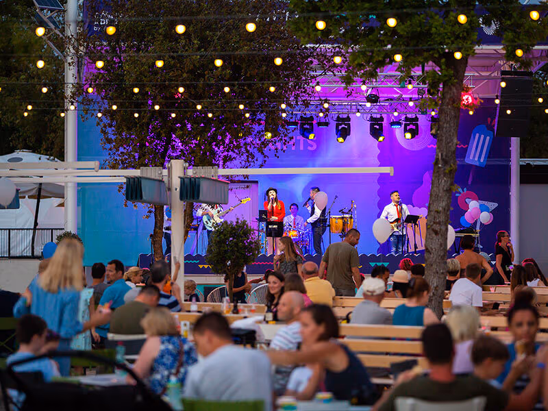 Publiek aan picknicktafels kijkt naar een liveband op het avondpodium van Camping Lanterna