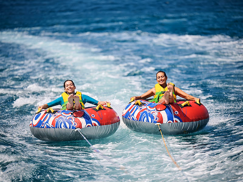 Twee watersporters op opblaasbare tubes achter een boot in zee bij Camping Lanterna