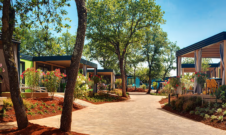 Autovrij wandelpad tussen kleurrijke accommodaties met pergolas in Maro Premium Village, Camping Lanterna