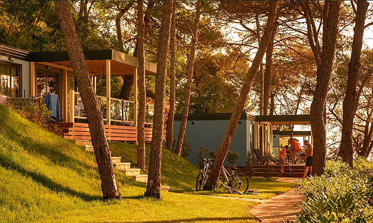 Accommodaties op een grasheuvel tussen de dennen in Marbello Village bij avondlicht, Camping Lanterna
