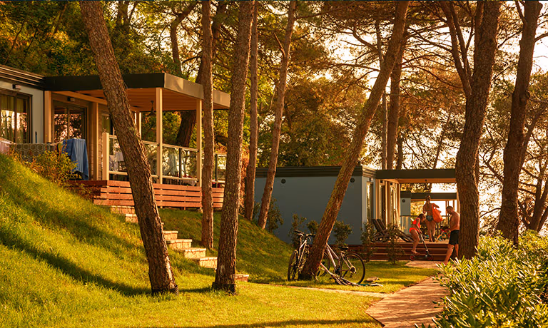 Accommodaties op een grasheuvel tussen de dennen in Marbello Village bij avondlicht, Camping Lanterna